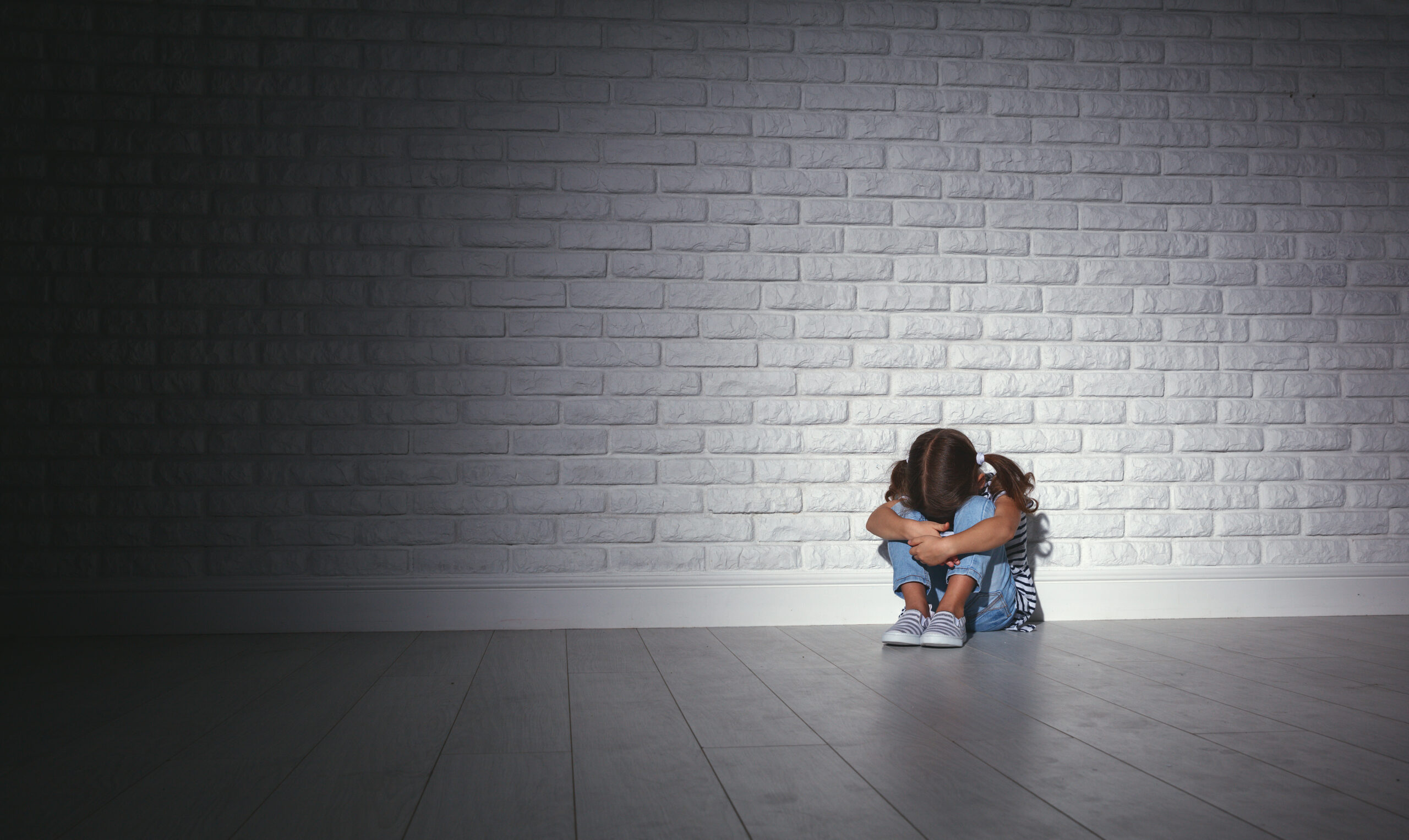 young girl curled up against a large bare gray well